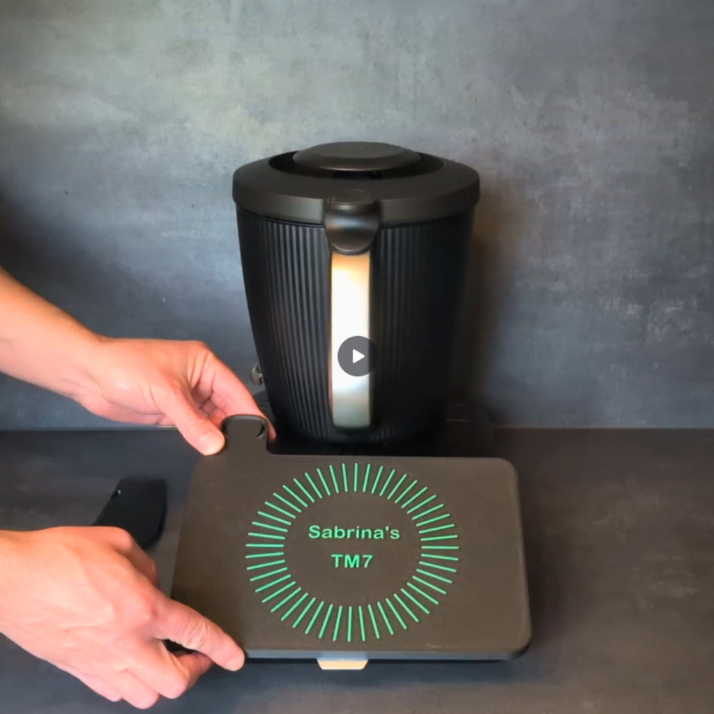 TM7 Displayschutz mit Wunschtext im Classic-Linien-Design. Gezeigt wird das Aufsetzen der Displayabdeckung auf den Thermomix TM7 sowie das Einsetzen des Spatels in den integrierten Spatelhalter.